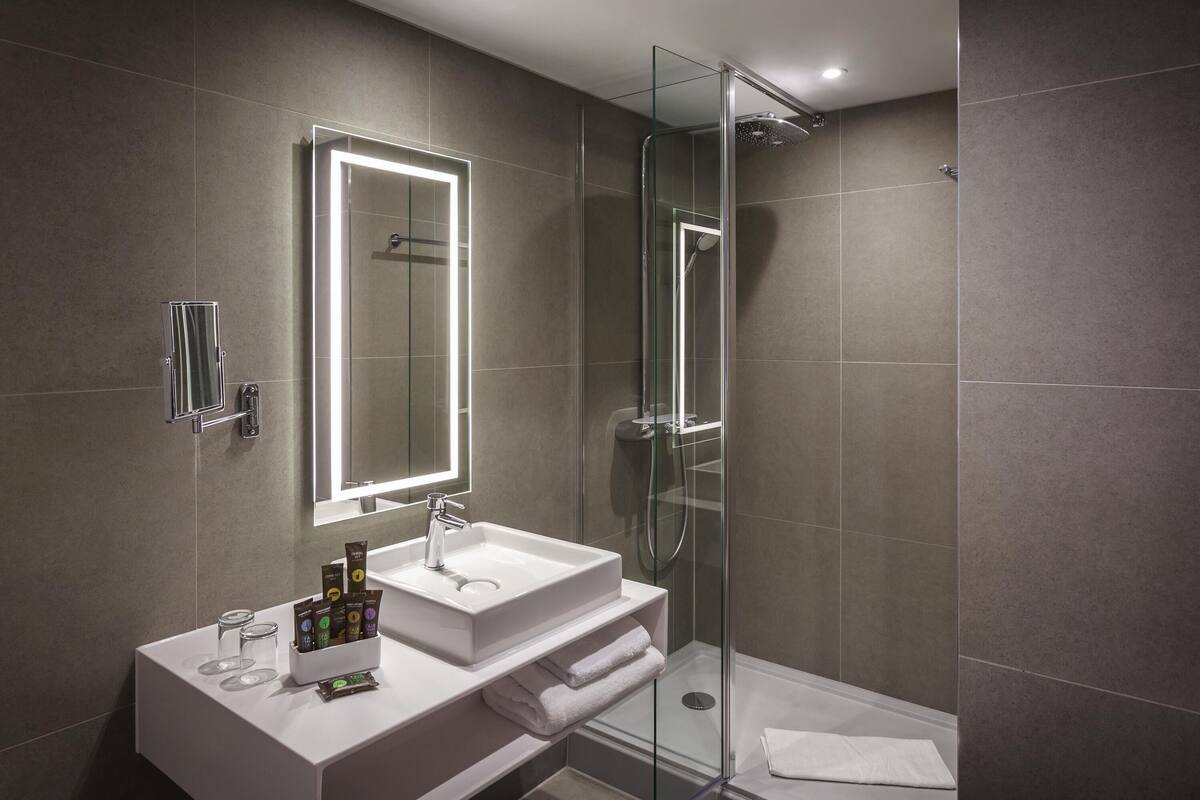A modern bathroom with a glass-enclosed shower, a large mirror, and a white vanity with toiletries.