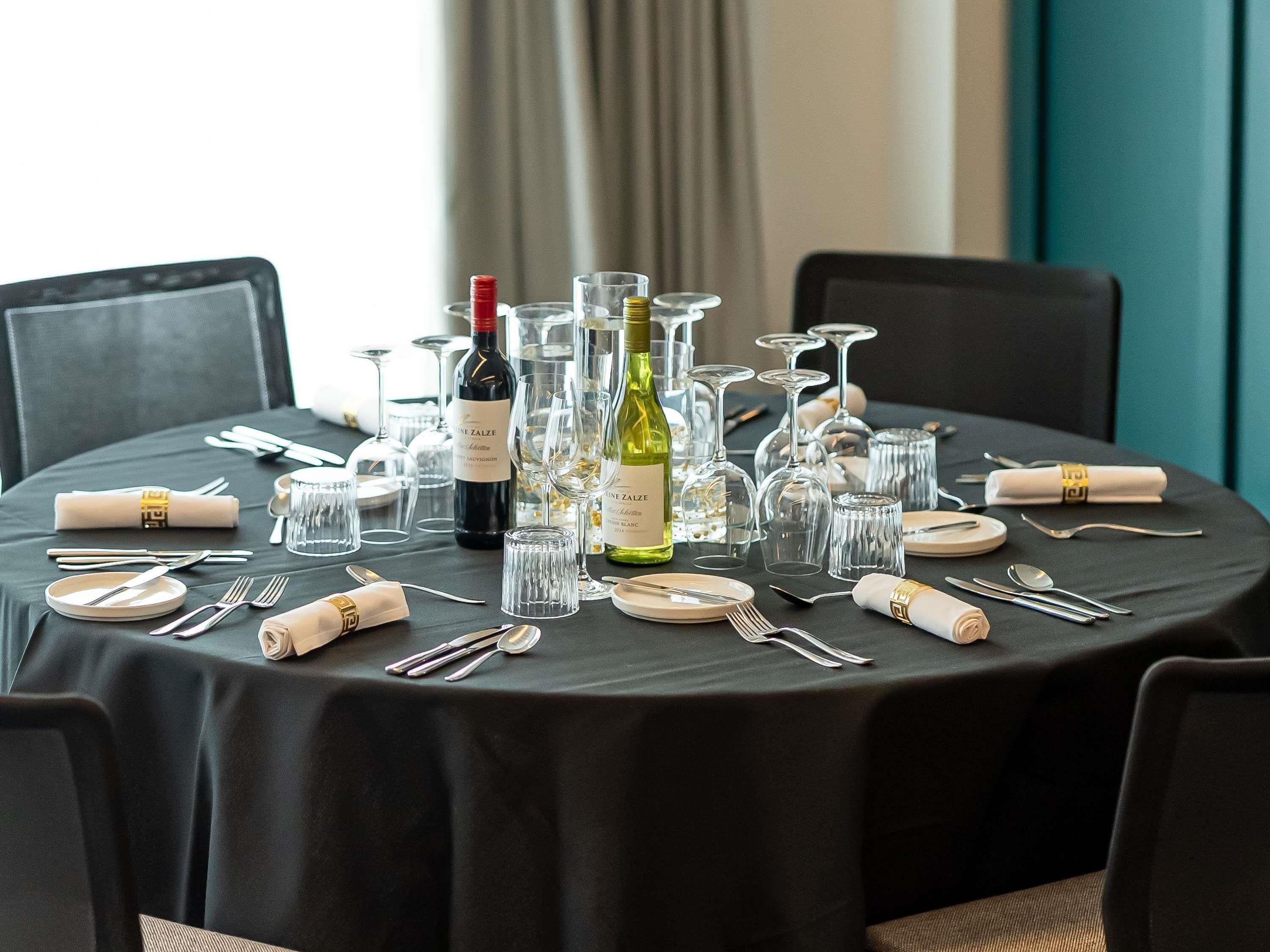 A round table set for dining with wine bottles, glasses, and cutlery.