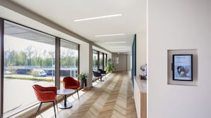 A modern interior with large windows, a herringbone wood floor, and red chairs. - Novotel Cambridge North (Cambridge)