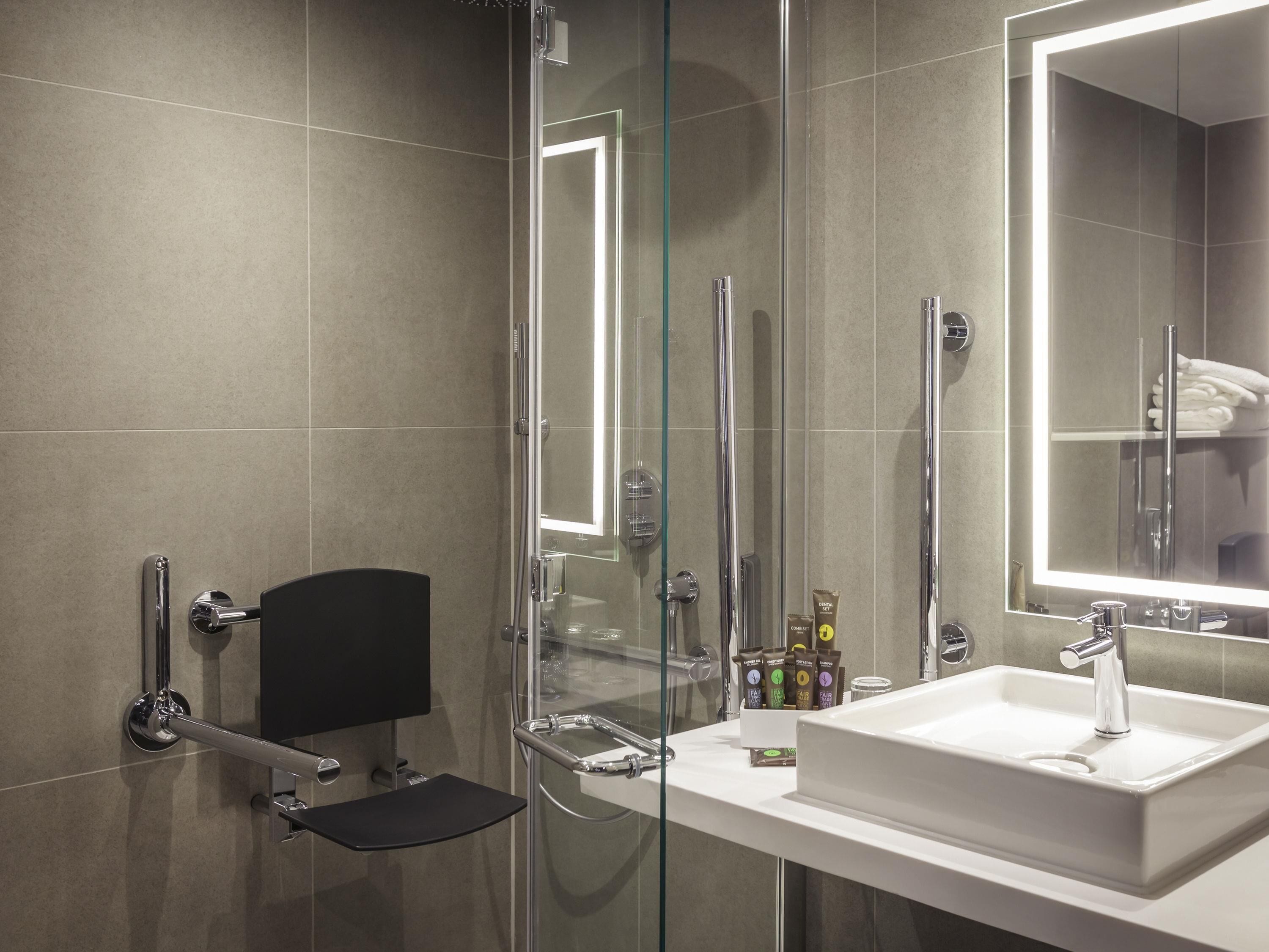 Ein modernes Badezimmer mit einer gläsernen Duschkabine, einem weißen Waschbecken und einem großen Spiegel.