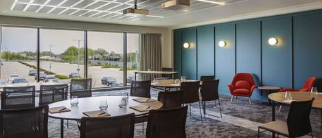Une salle de conférence équipée de tables, de chaises, d’un projecteur et offrant une vue sur un parking grâce à de grandes fenêtres.