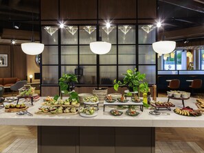 A buffet setup with various food items, a potted plant, and modern lighting fixtures. - Novotel Cambridge North (Cambridge)