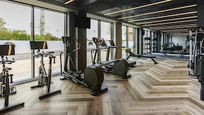 A modern gym with exercise equipment, large windows, and a herringbone floor pattern. - Novotel Cambridge North (Cambridge)