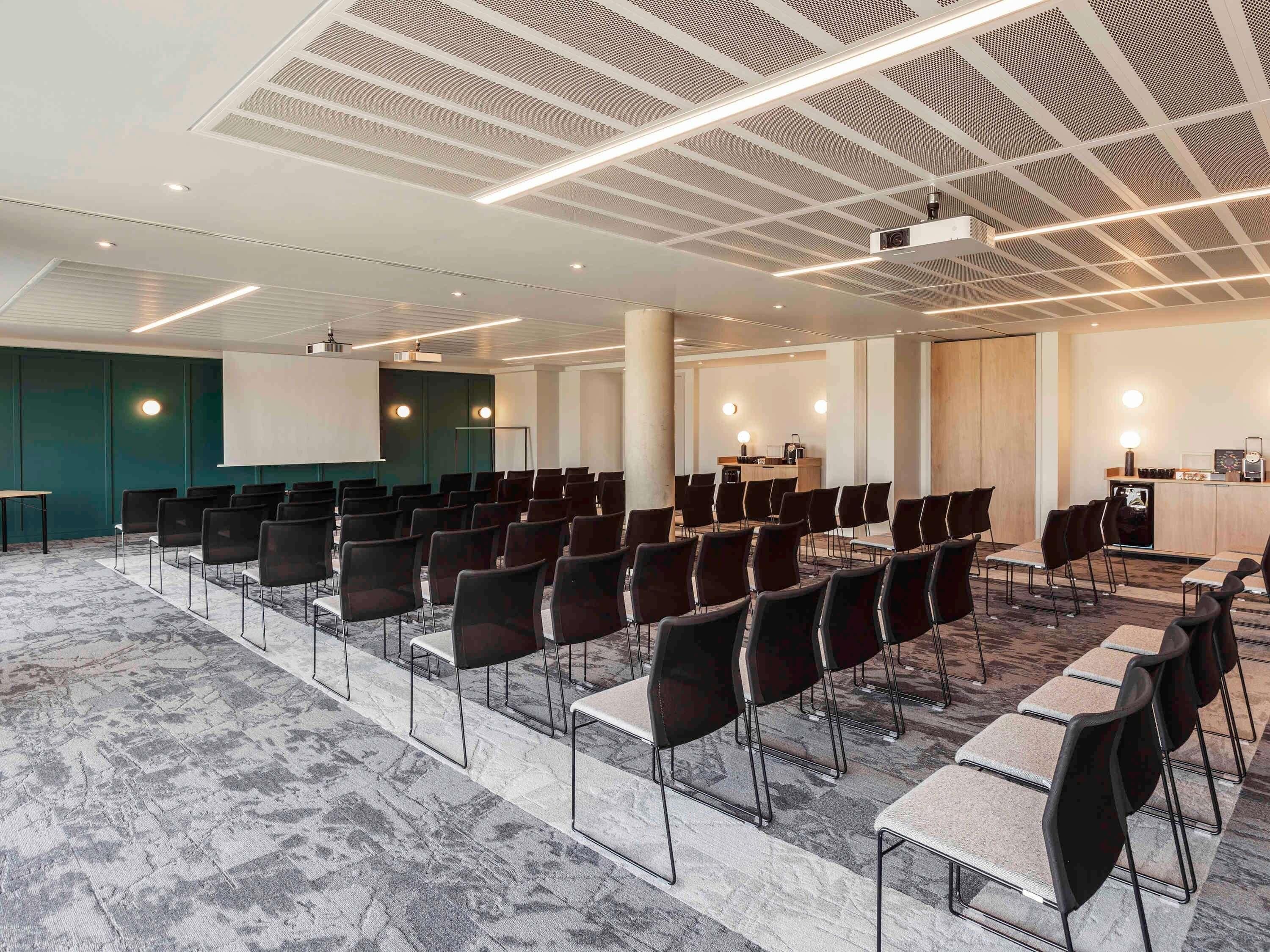 Una sala conferenze con file di sedie e tavoli, un proiettore e uno schermo per presentazioni.