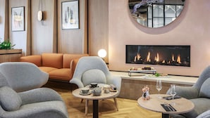 A modern lounge area with a fireplace, comfortable seating, and a small table with drinks and snacks. - Novotel Cambridge North (Cambridge)