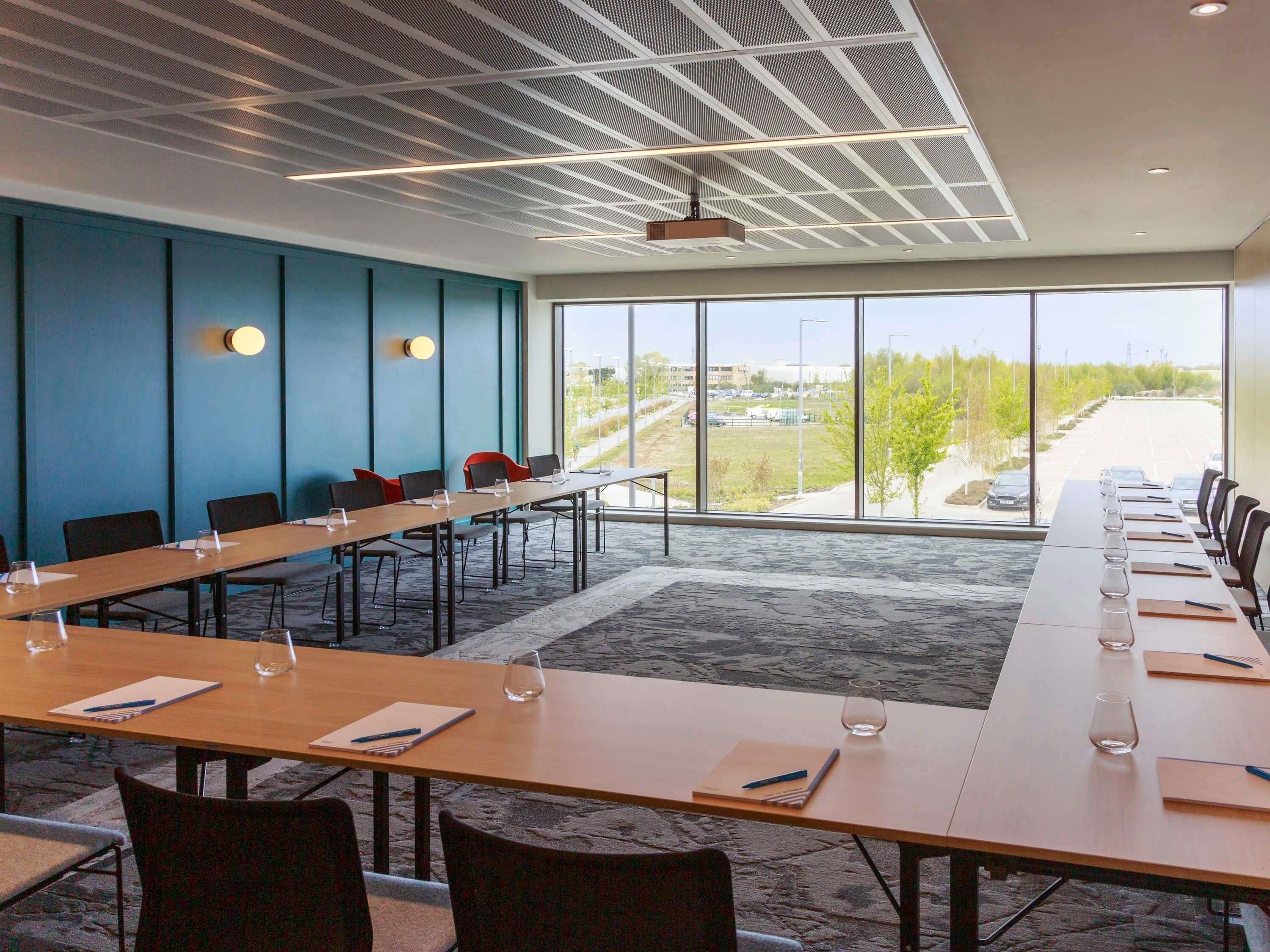 Uma sala de conferências com uma mesa comprida, cadeiras e uma grande janela com vista para o exterior.