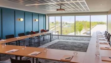 Uma sala de conferências com uma mesa comprida, cadeiras e uma grande janela com vista para o exterior.