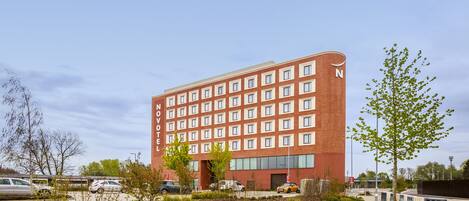 A modern hotel with a red brick facade, multiple windows, and a parking lot with cars.