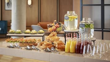 Un bufé con diversos alimentos, como sándwiches, pasteles y fruta. También hay varias botellas de bebidas y vasos sobre la mesa.