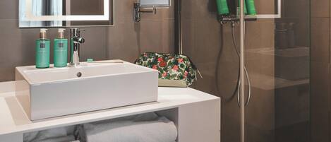 A modern bathroom with a white sink, mirror, and shower. There are toiletries on the sink and a towel rack with towels.
