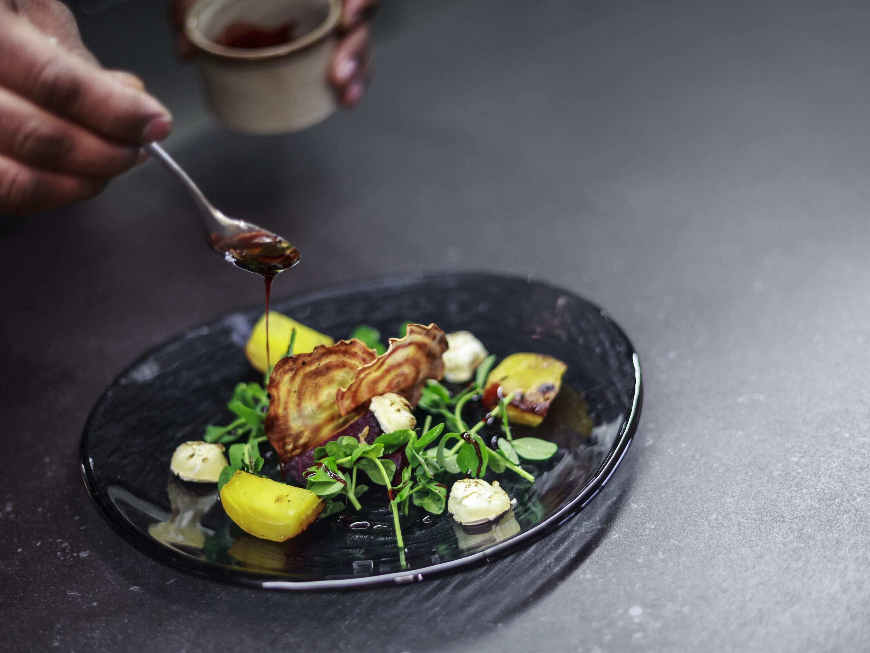 A plate of food with a spoon pouring sauce, set on a dark surface.