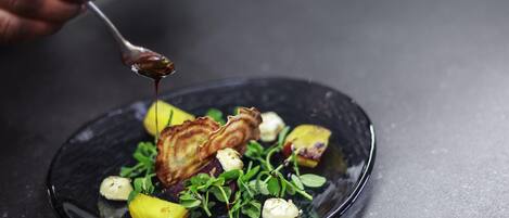 A plate of food with a spoon pouring sauce, set on a dark surface.