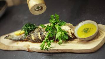 Pescado a la parrilla sobre una tabla de madera, acompañado de salsa y decoración de perejil.