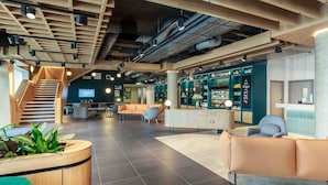 A modern hotel lobby with a staircase, seating areas, and a reception desk. - Novotel Cambridge North (Cambridge)