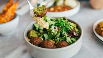 A bowl of falafel with a side salad and a spoon lifting falafel.
