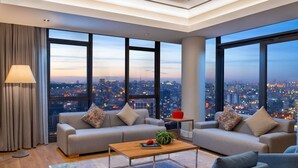 A modern living room with a sofa set, a coffee table, and a view of a cityscape at dusk. - Mövenpick Living Istanbul West (Istanbul)