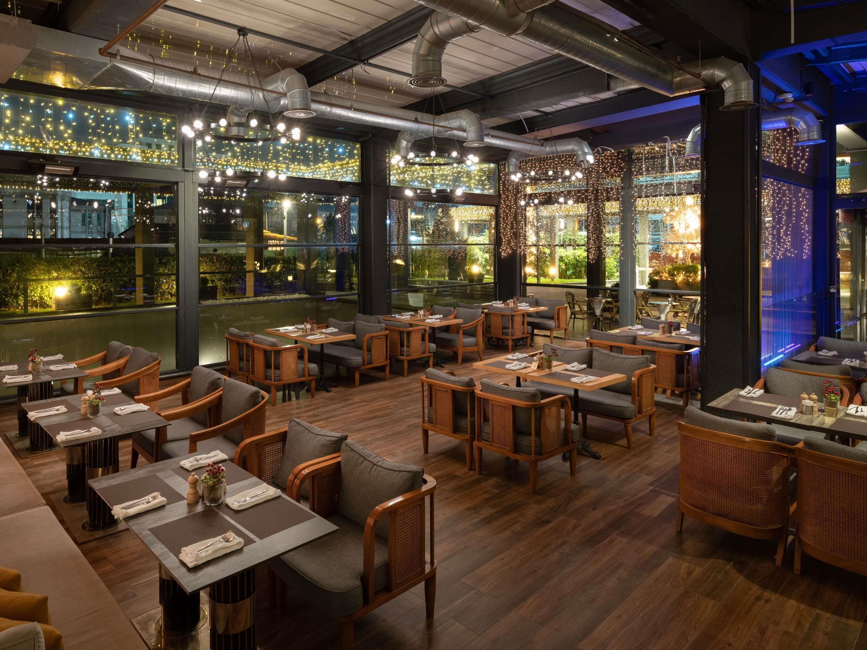 Ein Restaurant mit Holztischen und großen Fenstern mit Blick auf eine Stadtlandschaft.