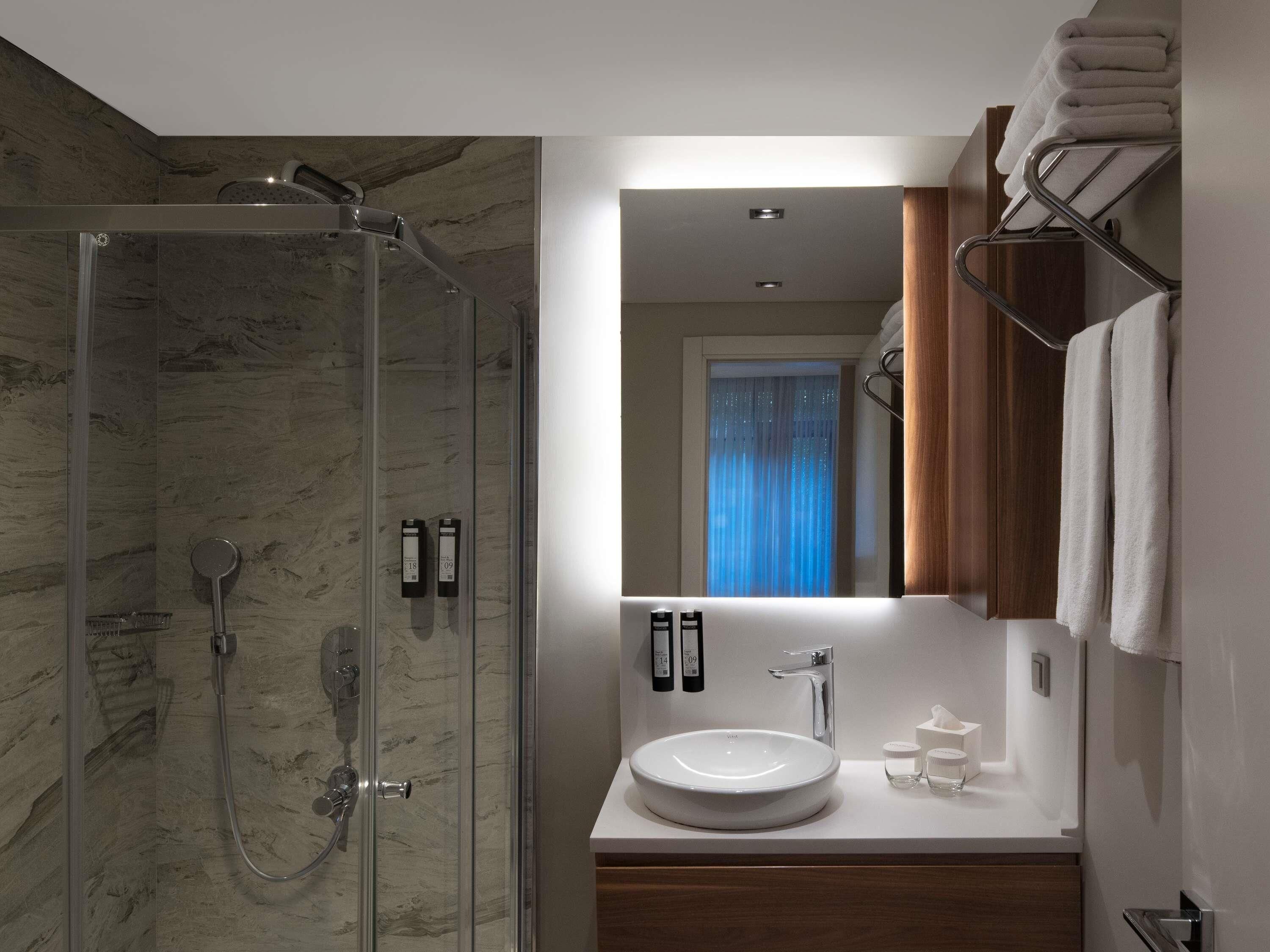 Une salle de bain moderne avec une douche à parois de verre, un lavabo blanc et un miroir au-dessus.