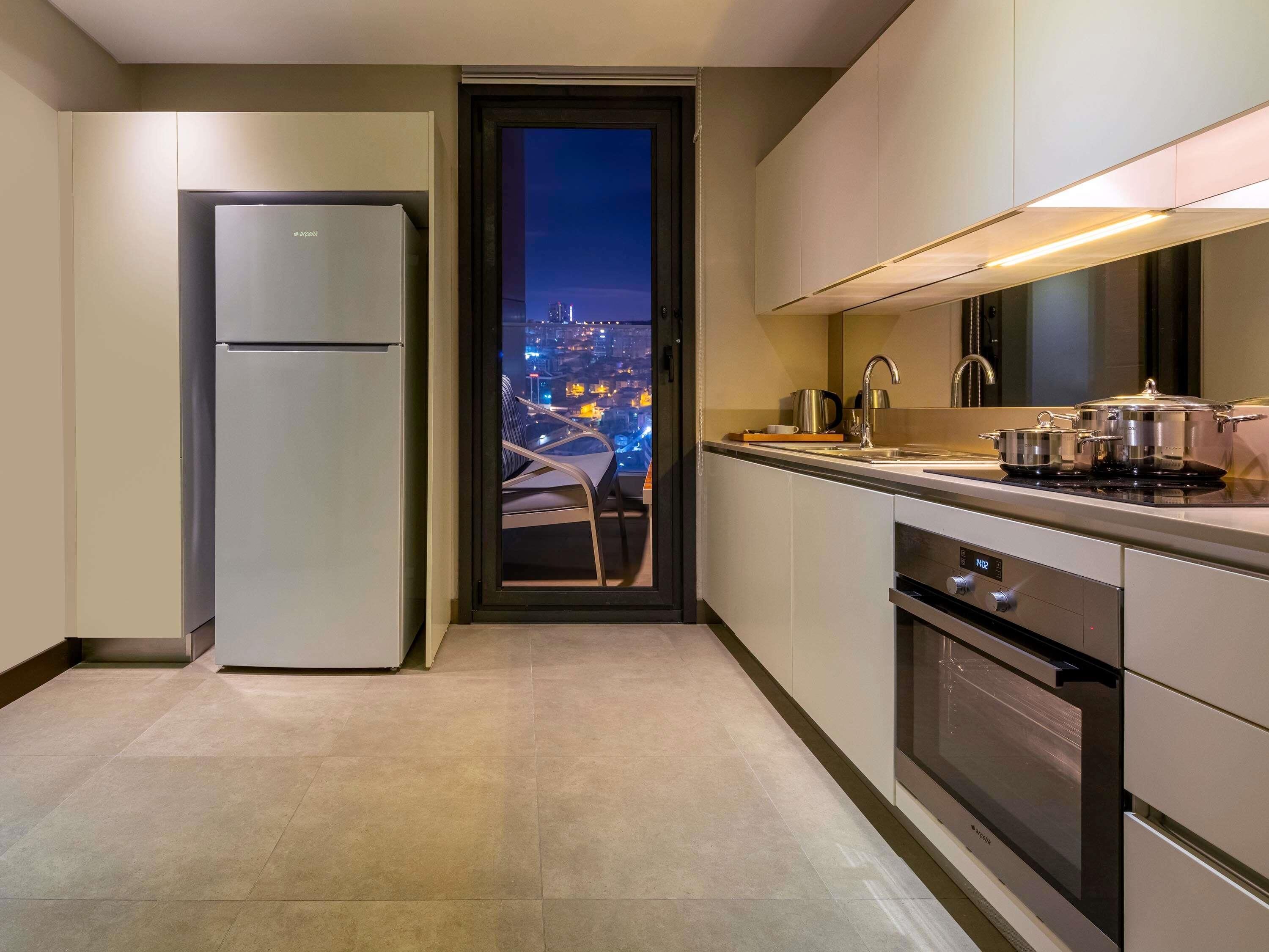 A modern kitchen with a built-in oven, a refrigerator, and a view of a cityscape at night.