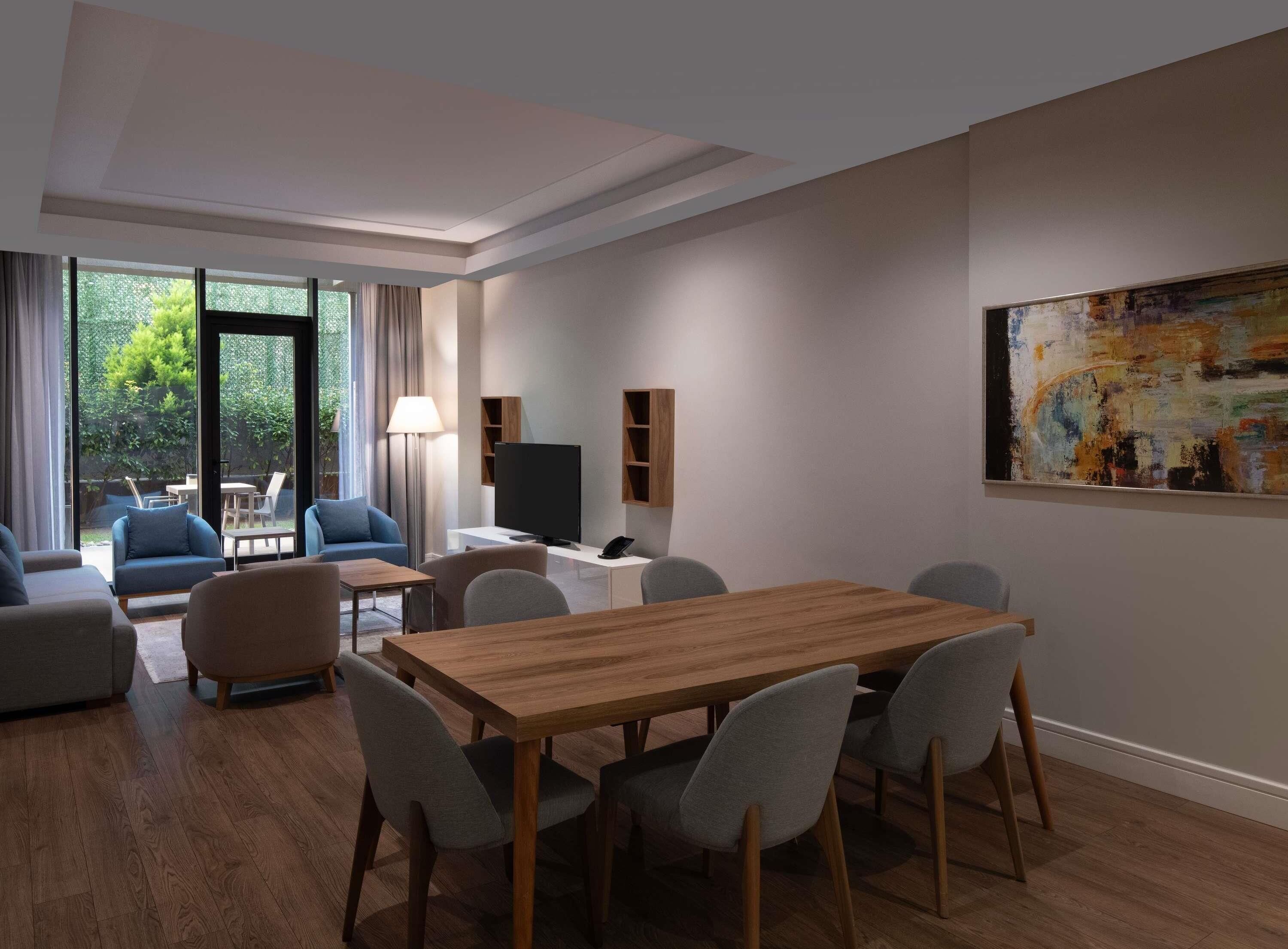 A modern hotel room with a dining area, a TV, and a painting on the wall.