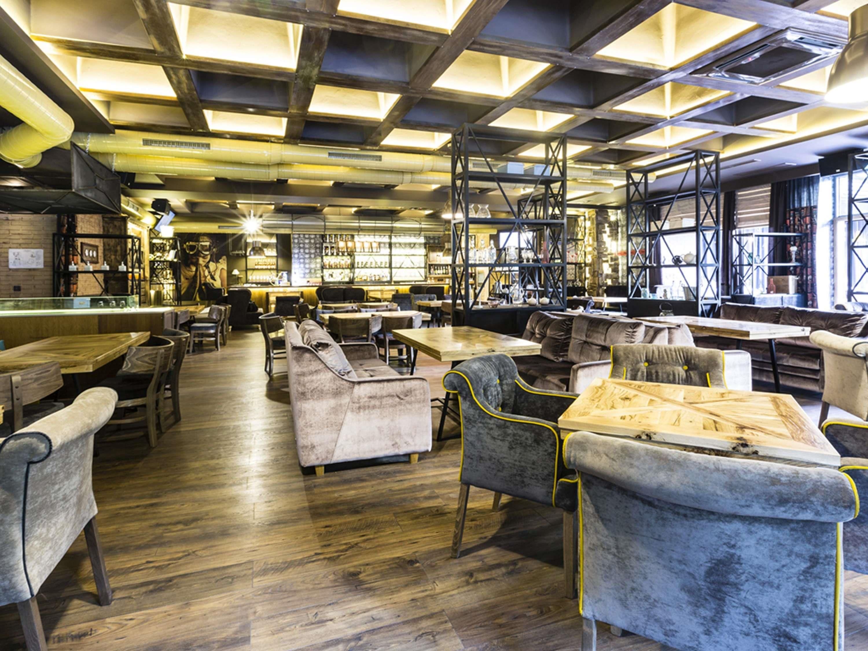 A spacious restaurant with high ceilings, exposed beams, and a variety of seating including tables and sofas.