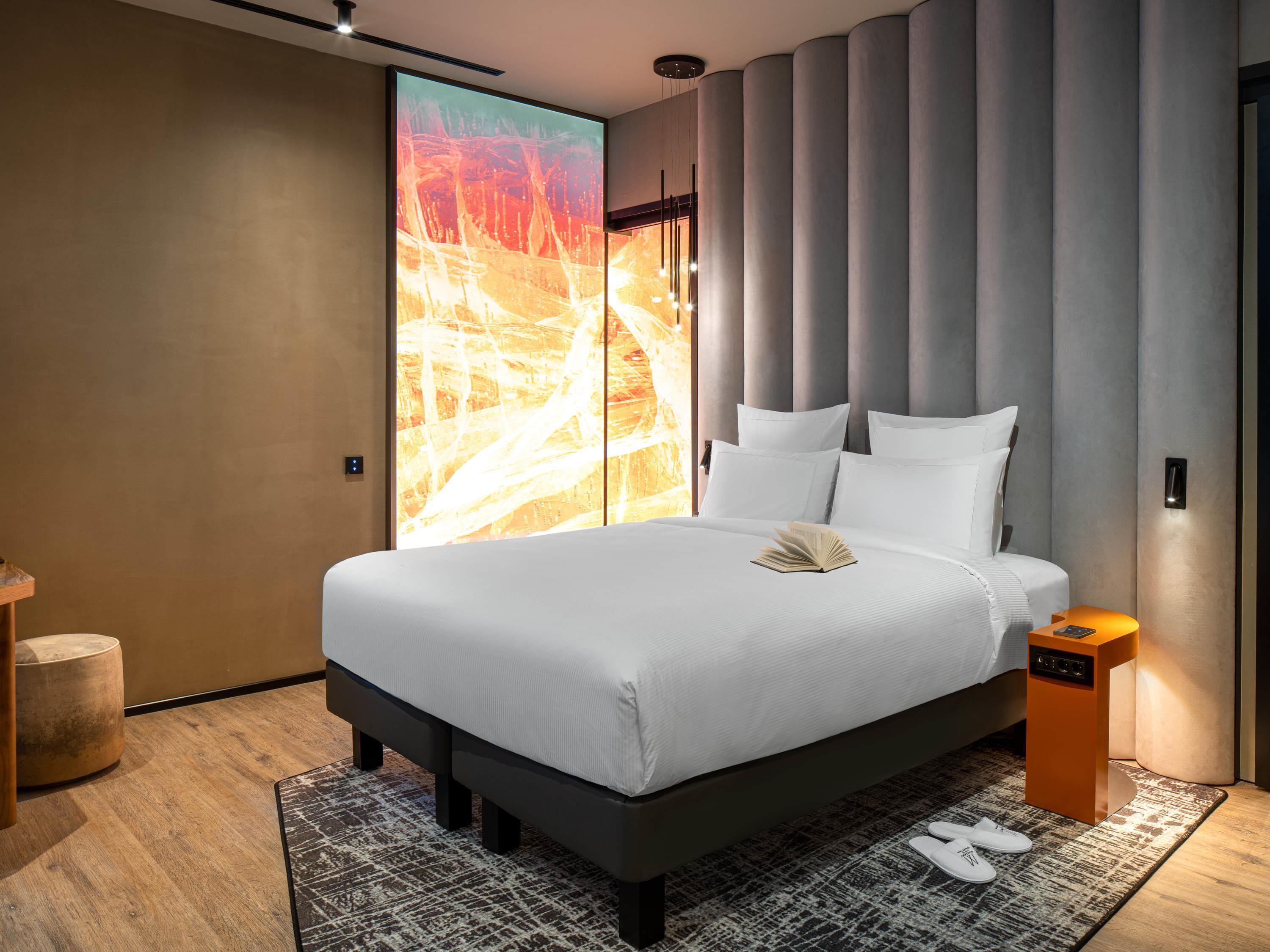 Una habitación de hotel moderna con una cama grande, una mesita de noche y un amplio ventanal con vistas.