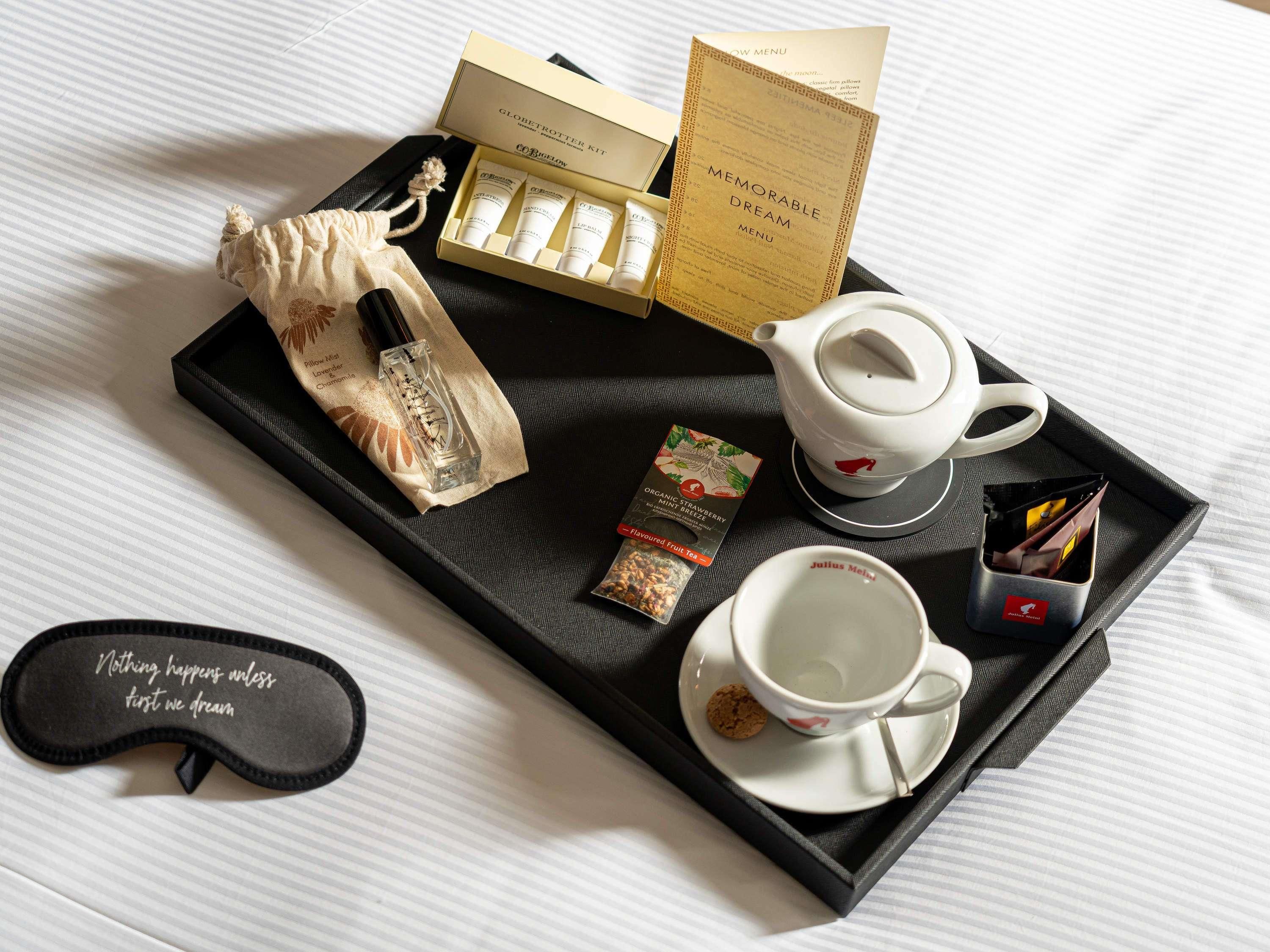 A tray with a tea set, a pack of cigarettes, a small bottle, and a pillow with a motivational quote.