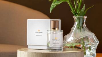 A perfume bottle with a box, a glass vase with flowers, and a wooden surface.