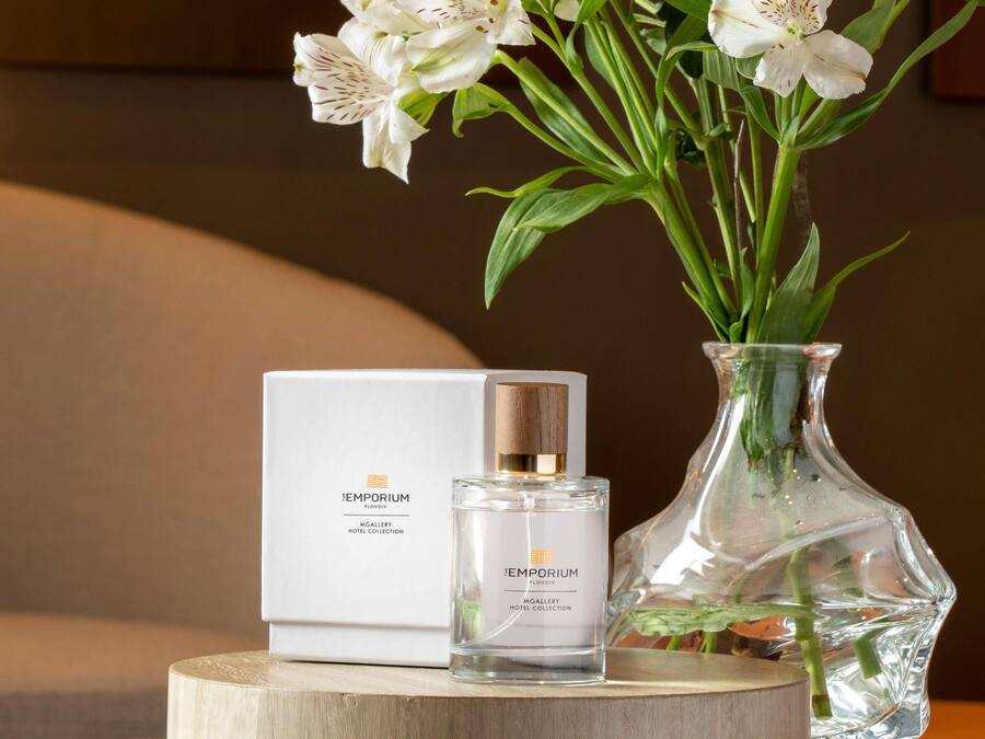 A perfume bottle with a box, a glass vase with flowers, and a wooden surface.