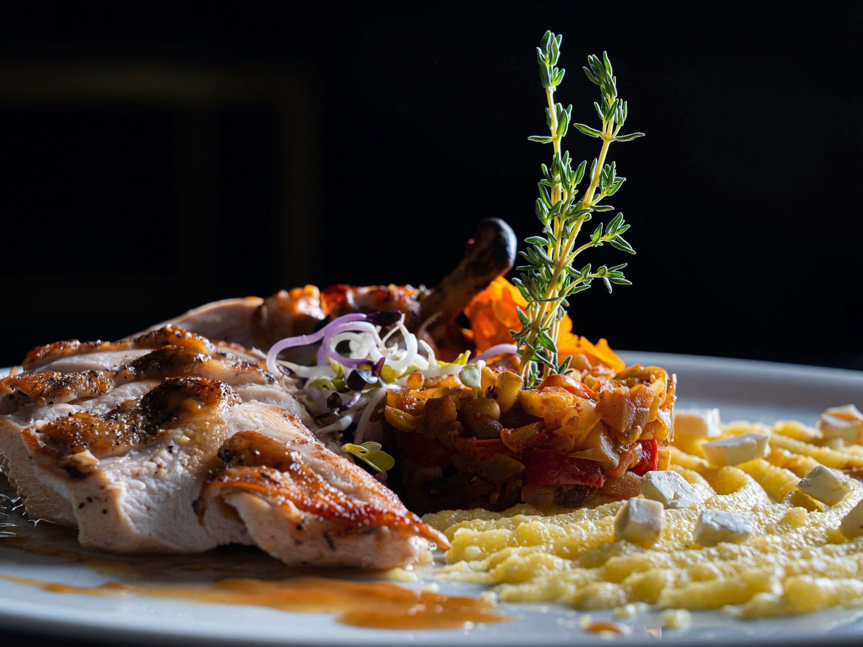 A plate of food with a roasted meat, vegetables, and a garnish of herbs.