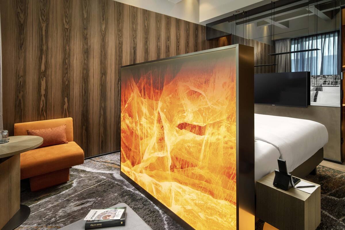 Una habitación de hotel moderna con una cama grande, un sofá, un televisor y una pared con textura similar a la madera.
