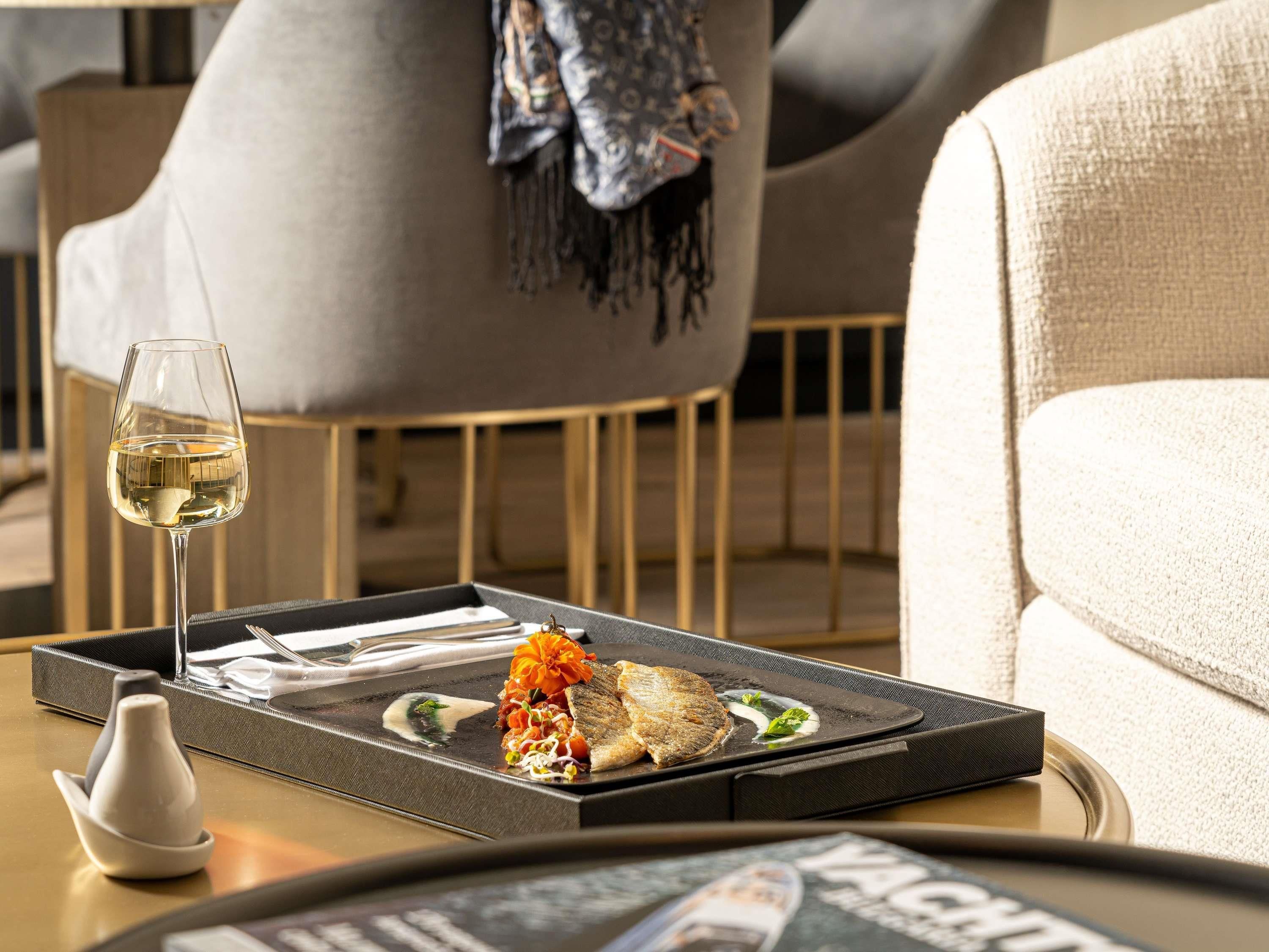 A dining table with a glass of white wine, a plate with food, and a remote control.