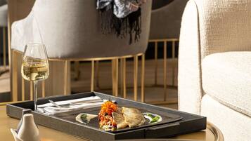 A dining table with a glass of white wine, a plate with food, and a remote control.