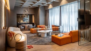 Un salon moderne avec des canapés orange, une table basse ronde et un coin repas séparé par une cloison en verre.
