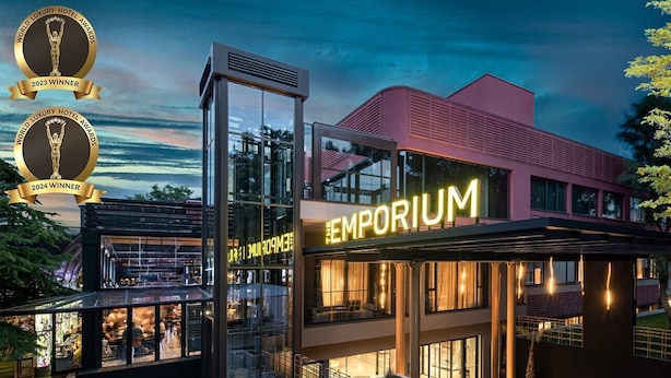 Un hôtel moderne, reconnaissable à son grand panneau « EMPORIUM », à sa façade en verre et à son espace extérieur aménagé en terrasse.