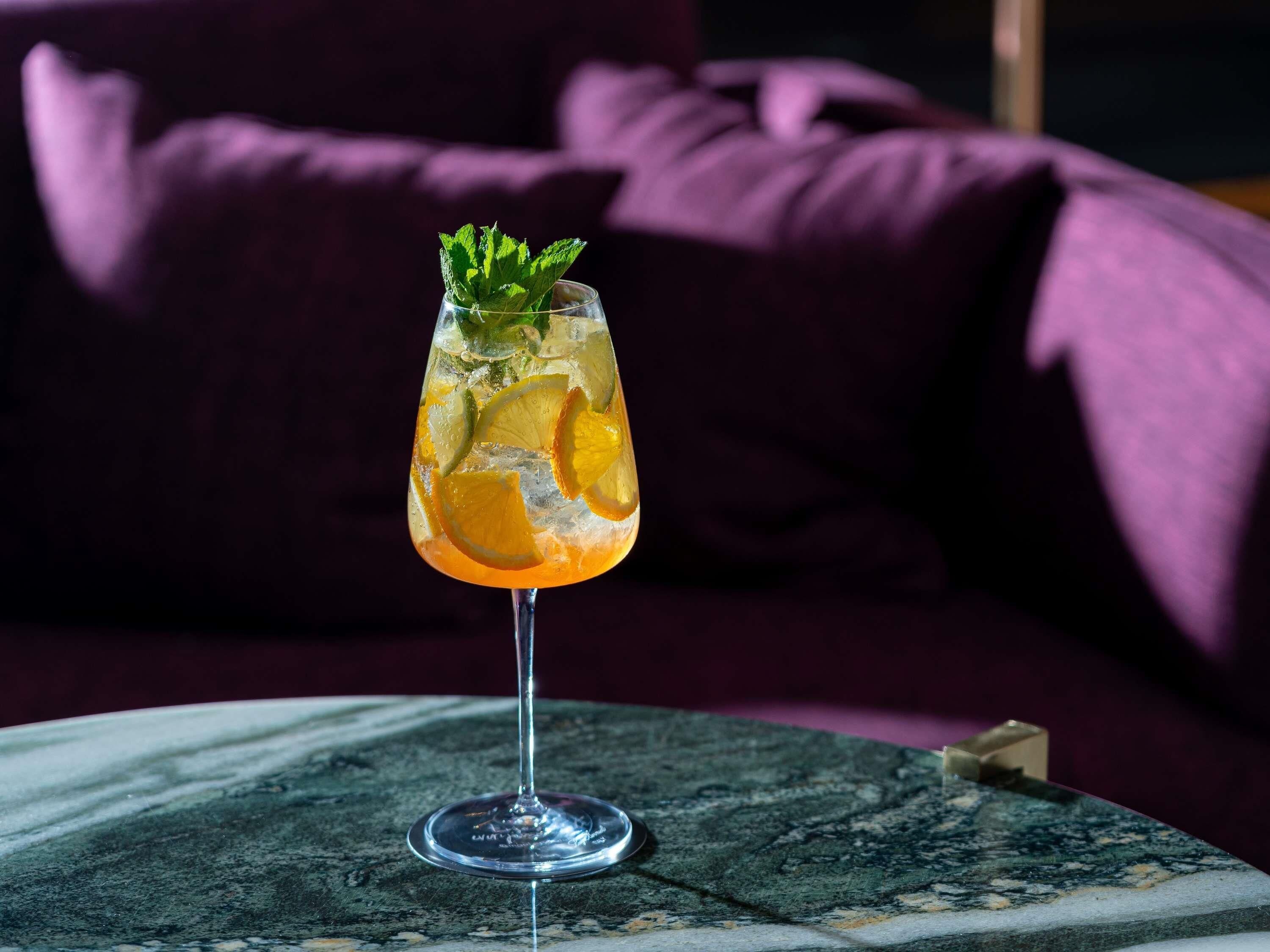 A cocktail glass with citrus slices and mint on a marble table.