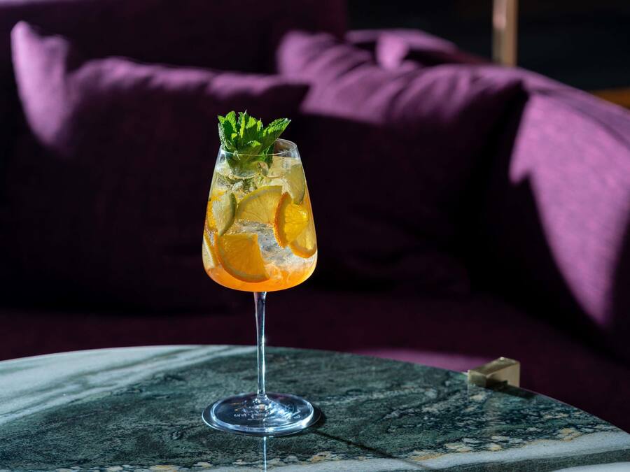 Et cocktailglas med citrusstykker og mynte på et marmorbord.