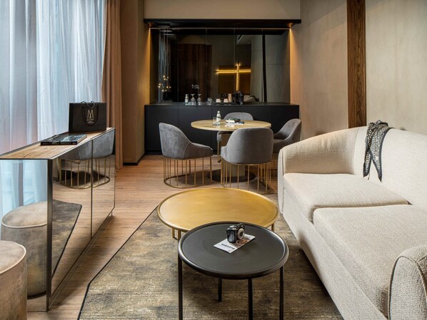 A modern hotel room with a sofa, two round tables, a coffee table, a desk, and a chair.
