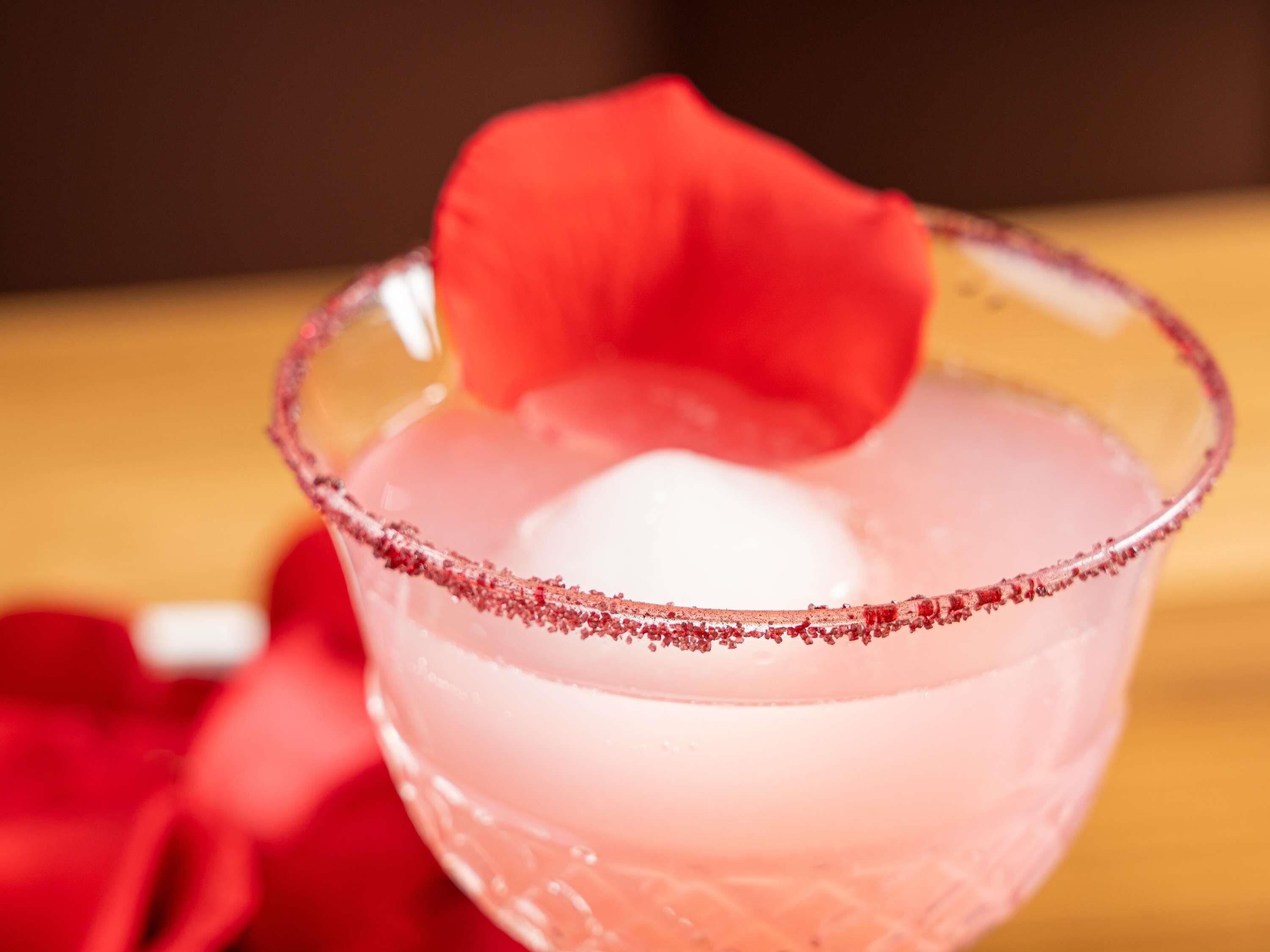 A cocktail in a glass with a salted rim and a rose garnish.
