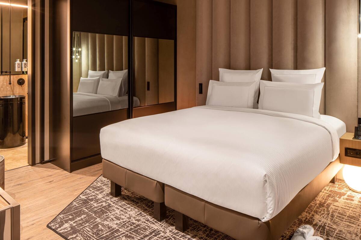 Quarto de hotel moderno com uma cama grande, um guarda-roupa, um espelho e uma mesa de cabeceira.