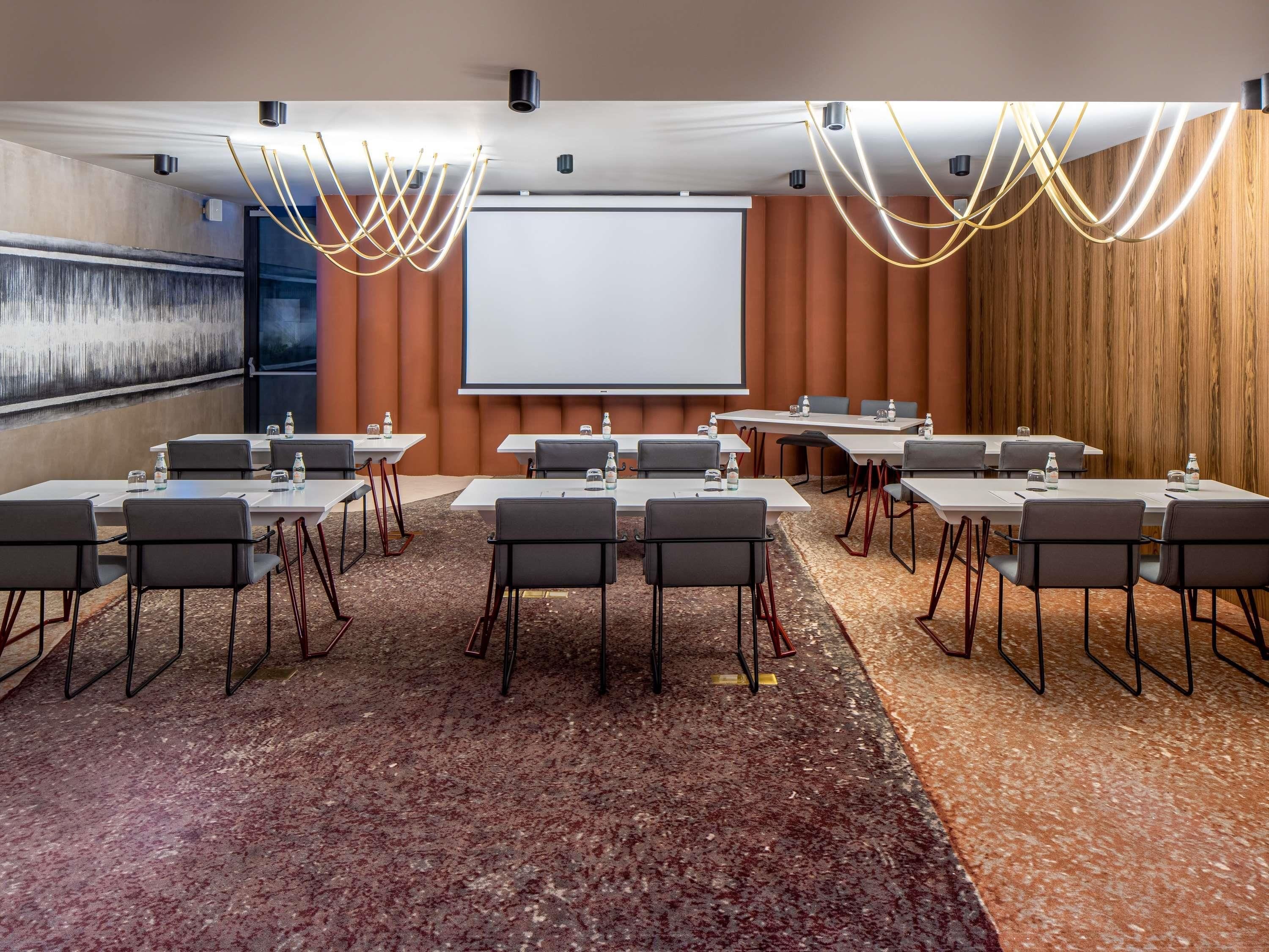 A conference room with a large screen, multiple tables, chairs, and a carpeted floor.