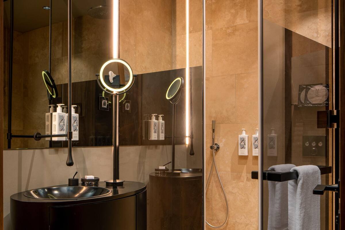 Un baño moderno con un lavabo redondo, un espejo con luz y una cabina de ducha de vidrio.
