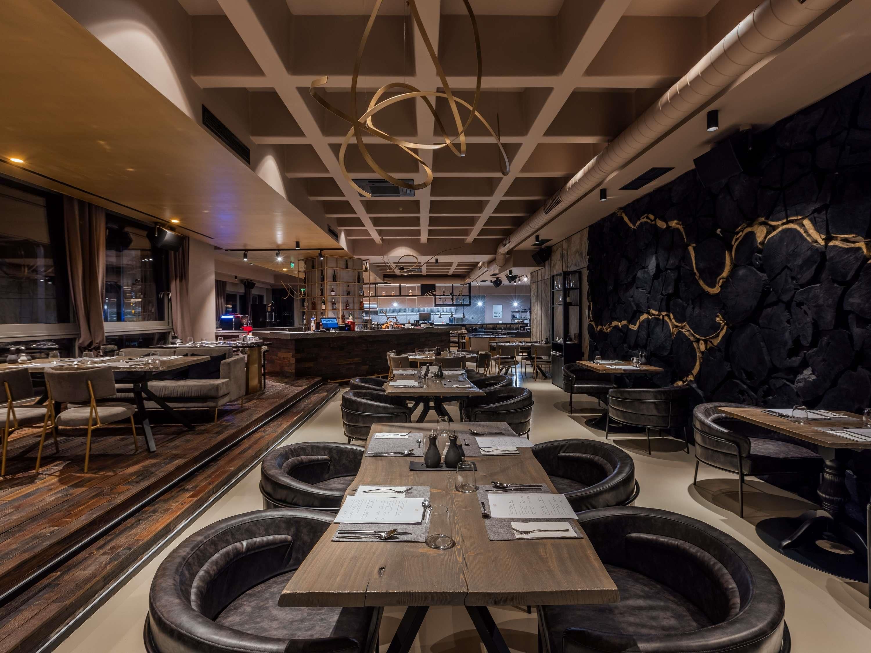 A modern restaurant interior with a central dining table, surrounding booths, and a kitchen in the background.