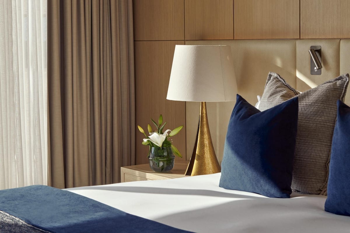 A hotel room with a bed, a nightstand with a lamp, and a vase with flowers.