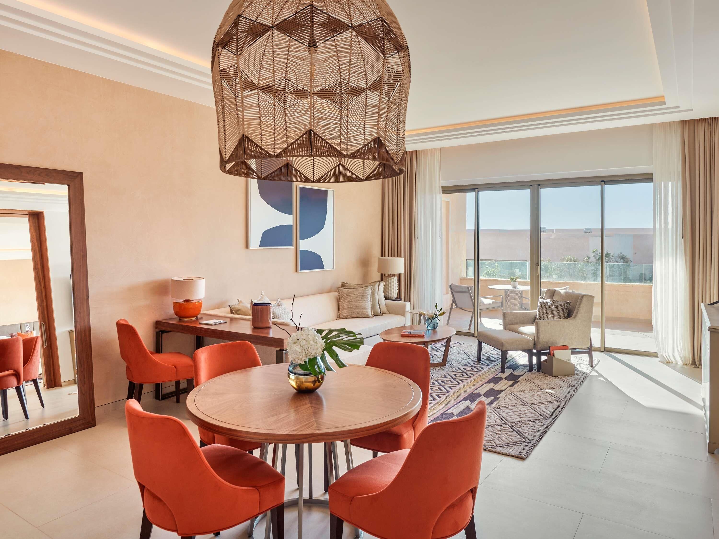 Una habitación de hotel moderna con comedor, sofá, un amplio ventanal con vistas y una lámpara colgante original.