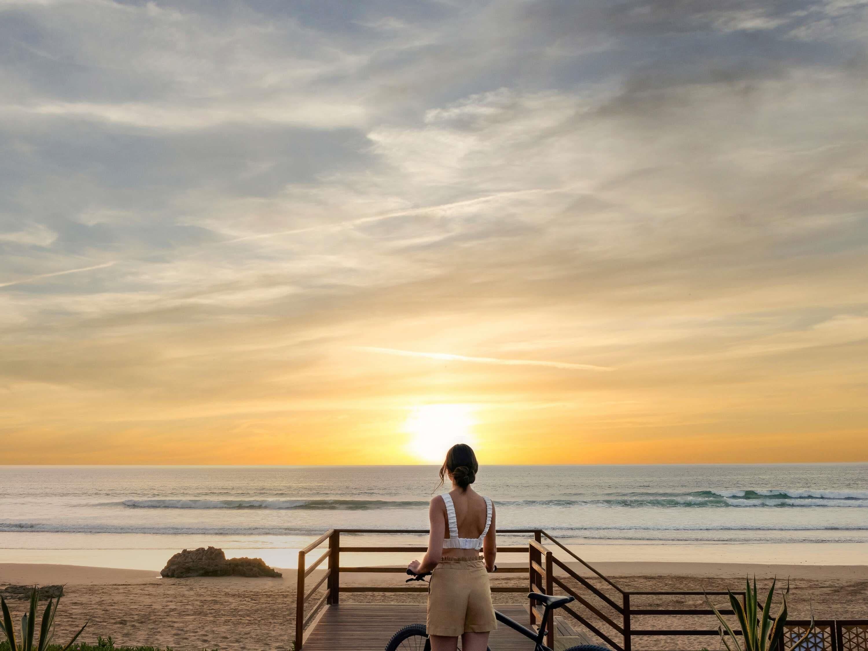 A person standing on a wooden deck overlooking the ocean at sunset.