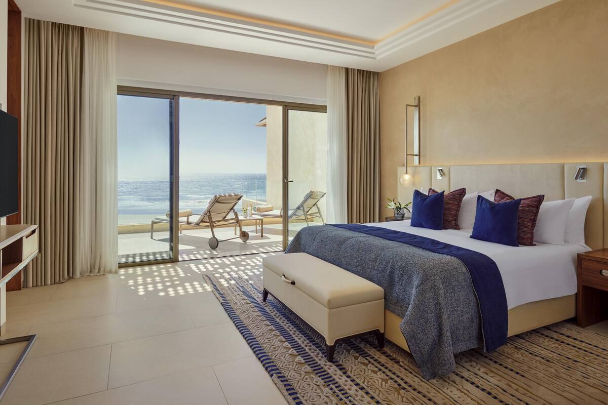 Habitación de hotel con una cama grande, televisión, escritorio y balcón con vista al océano.
