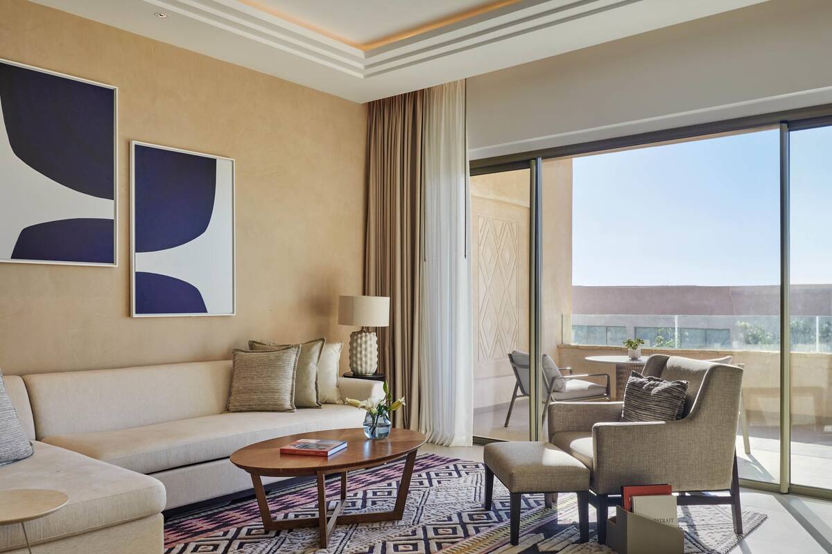Una habitación de hotel moderna con sofá, sillones, una mesita de centro y un ventanal con vistas.