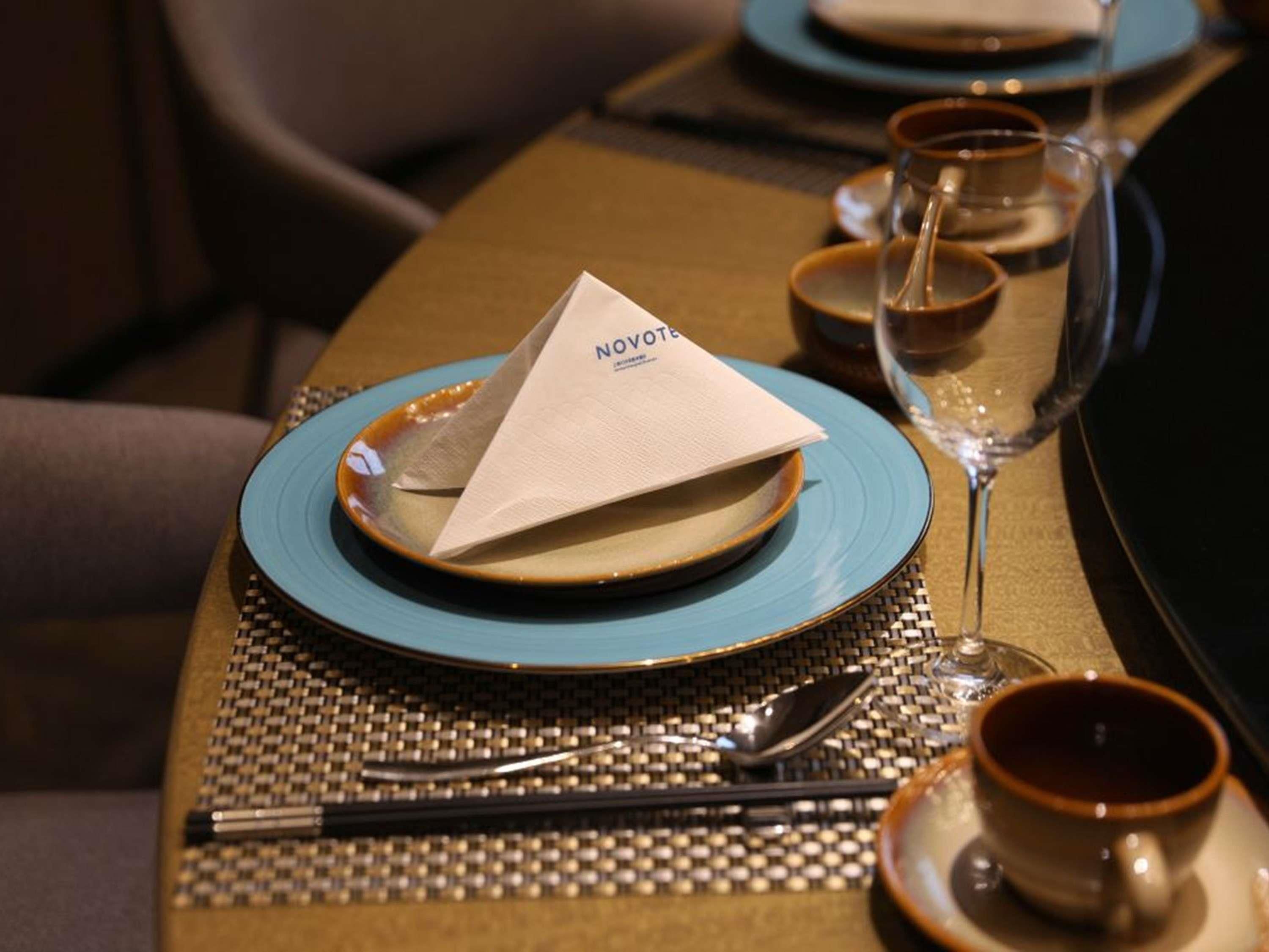 Une table dressée avec une assiette bleue, une serviette, une tasse et un verre.