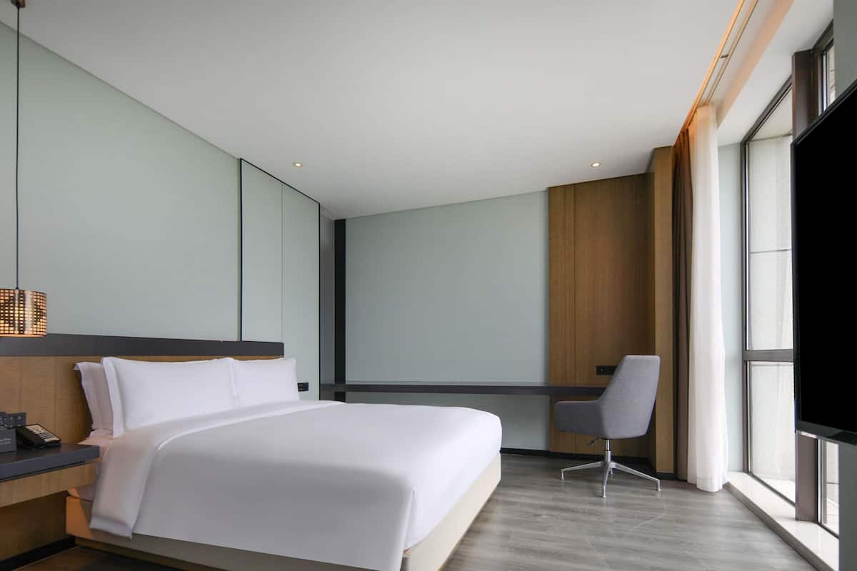 A modern hotel room with a large bed, a desk, and a chair.